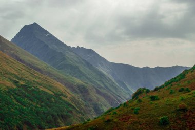 Kafkasya, bulutlu gökyüzü, dağ zirveleri ve yeşil yamaçları bulanık yağmurlu manzara