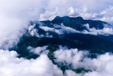 yukarıdan, tepe veya bir uçak, yerleşim, kısmen kümülüs bulutlar tarafından gizli bir ormanlık dağ Vadisi için göster