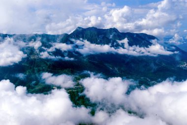 yukarıdan, tepe veya bir uçak, yerleşim, kısmen kümülüs bulutlar tarafından gizli bir ormanlık dağ Vadisi için göster