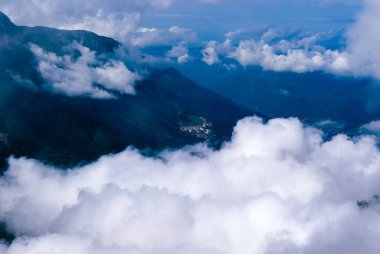 yukarıdan, tepe veya bir uçak, yerleşim, kısmen kümülüs bulutlar tarafından gizli bir ormanlık dağ Vadisi için göster