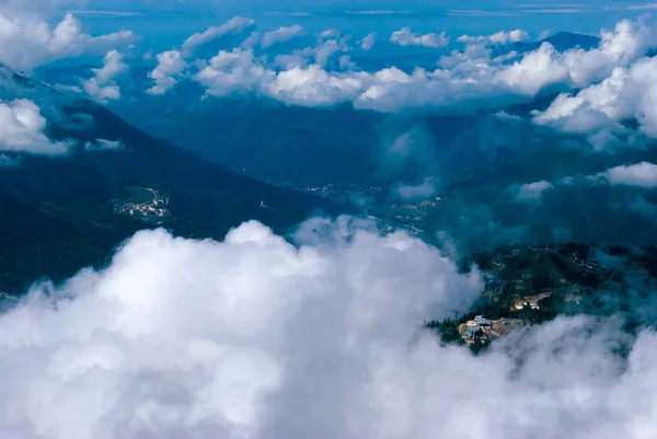 上から ピークまたは積雲の雲によって部分的に隠された集落の樹木が茂った山の谷に 飛行機から見る — ストック写真