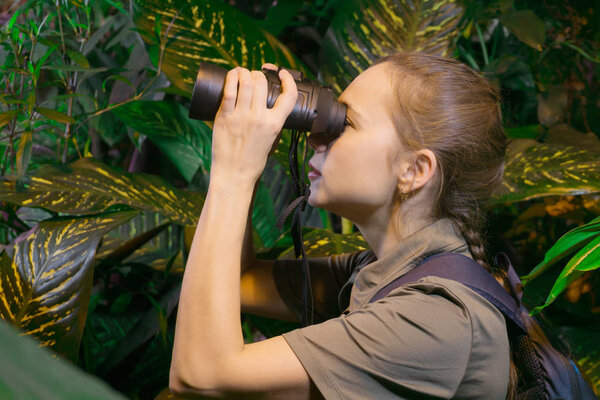traveler girl among the tropical forest looks into the distance through binoculars