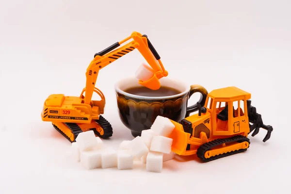 toy construction machines loads sugar into a real cup of coffee on a light backgroun