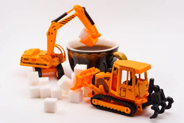 toy construction machines loads sugar into a real cup of coffee on a light background