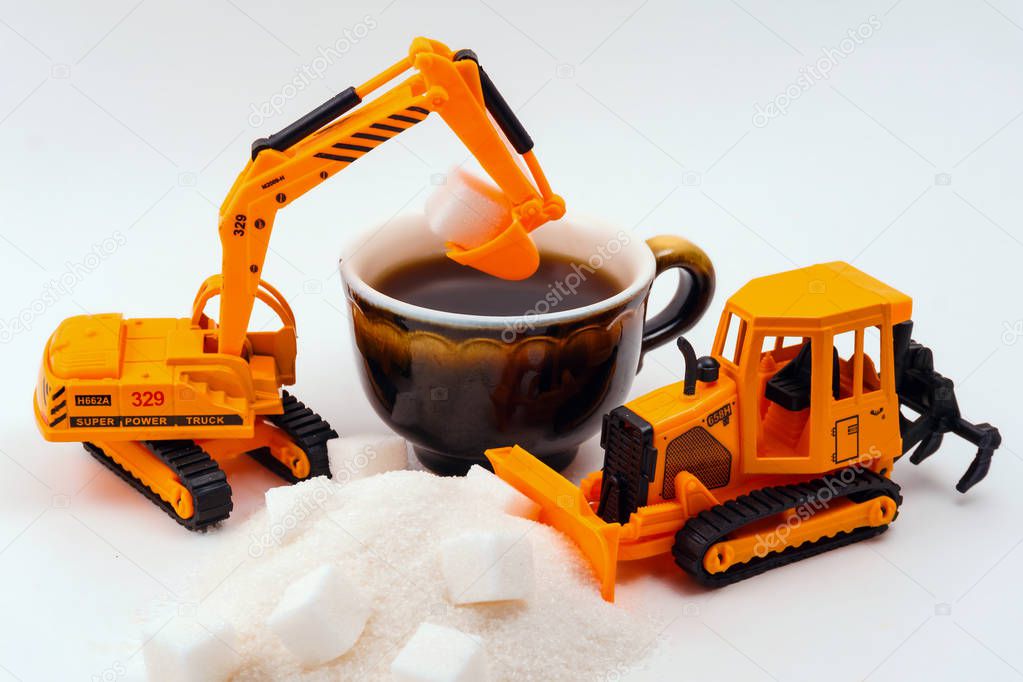toy construction machines loads sugar into a real cup of coffee on a light background