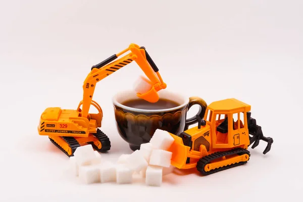 toy construction machines loads sugar into a real cup of coffee on a light background