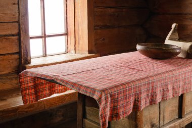 fragment of the interior of an old peasant log cabin - a table with wooden dishes, and handmade woven tablecloth clipart