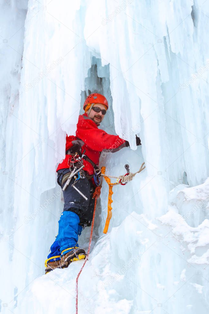 ice climber on a vertical wall of a frozen waterfall among huge icicles