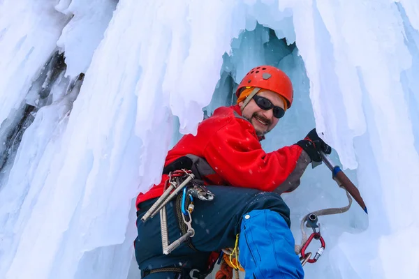 Lächelnder Männlicher Bergsteiger Mit Eispickel Zwischen Eiszapfen Eines Gefrorenen Wasserfalls — Stockfoto