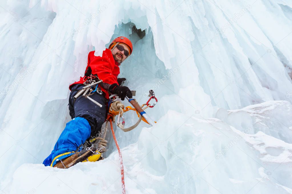 ice climber on a vertical wall of a frozen waterfall among huge icicles