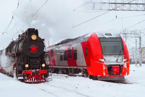 Locomotiva a vapor e moderno trem de várias unidades estão nas proximidades em — Fotografia de Stock