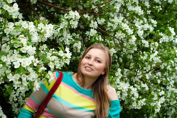 Mulher sorridente no fundo de uma macieira florescente — Fotografia de Stock