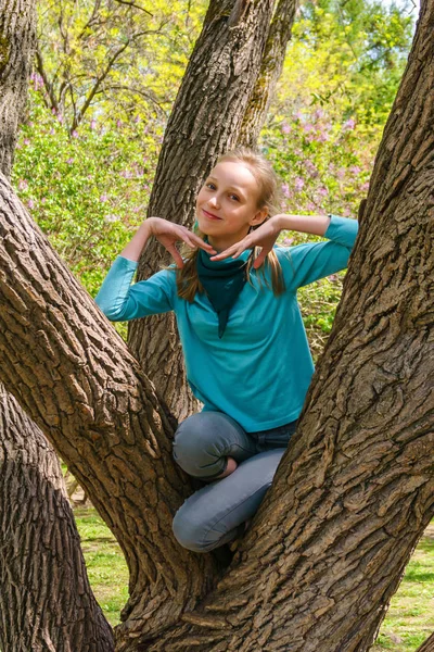 Улыбающаяся девочка-подросток залезла на дерево в парке — стоковое фото