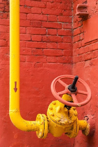 Gul rörledning med ventil mot röd vägg — Stockfoto