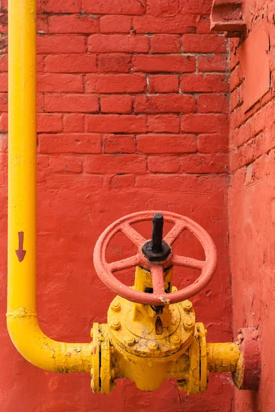 Žluté potrubí s ventilem proti červené stěně — Stock fotografie