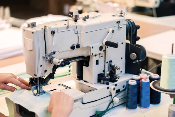 industrial overlock sewing machine and hands of seamstress at work in the garment factory
