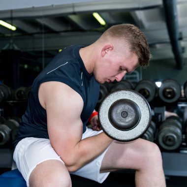 Adam spor salonunda dambıllarla egzersiz yapıyor.