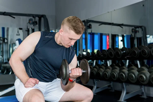 Adam spor salonunda dambıllarla egzersiz yapıyor.