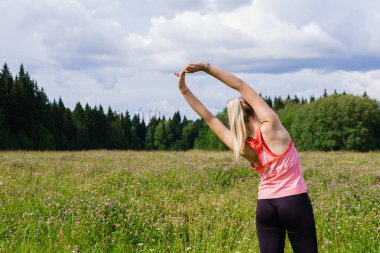 c dışında bir çayırda uzanan egzersizleri yapan genç kadın