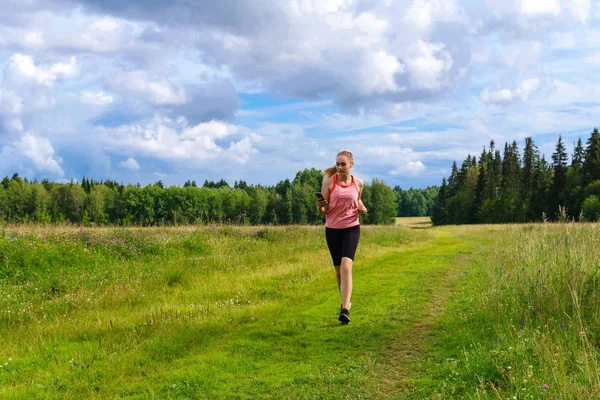 Jonge vrouw joggen in de weide en luisteren naar muziek op het hoofd — Stockfoto