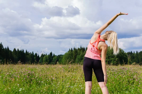 c dışında bir çayırda uzanan egzersizleri yapan genç kadın