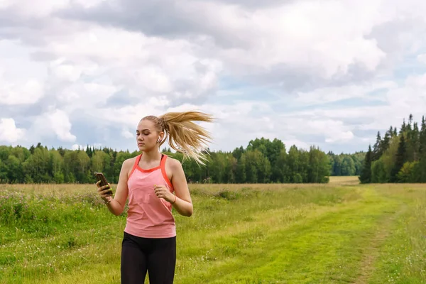 Jeune femme jogging dans la prairie et écouter de la musique sur la tête — Photo