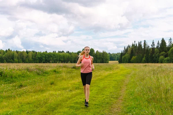 Jonge vrouw joggen in de weide en luisteren naar muziek op het hoofd — Stockfoto