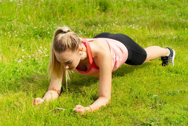 Молодая женщина делает упражнения доски на траве — стоковое фото