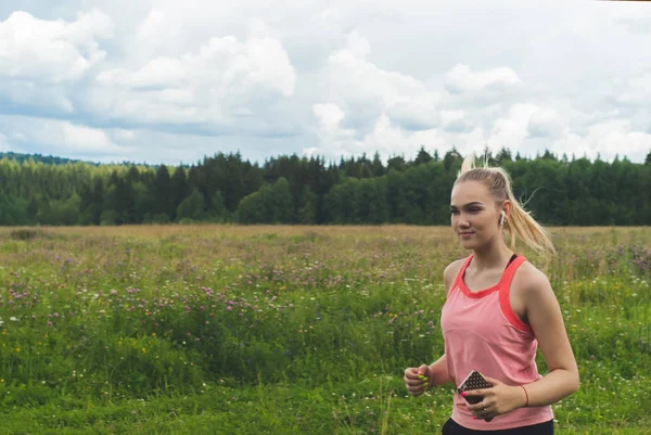 Jonge vrouw joggen in de weide en luisteren naar muziek op het hoofd — Stockfoto