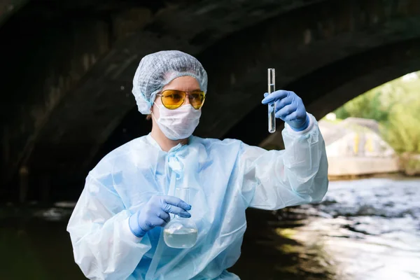 Ecologista femenina examina un tubo de ensayo con agua de un riv de la ciudad — Foto de Stock