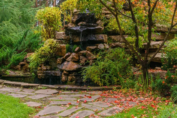 Lawn among decorative bushes with a path and artificial rock wit — Stock Photo, Image