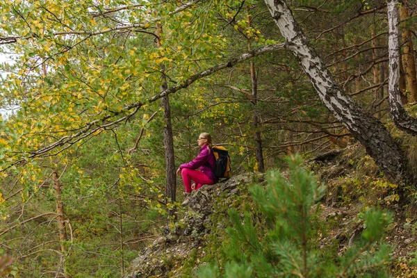 Mulher jovem caminhante senta-se descansando em um penhasco entre os inimigos da montanha — Fotografia de Stock