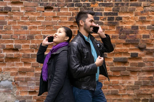 young man and woman stand nearby back to back, talking on their