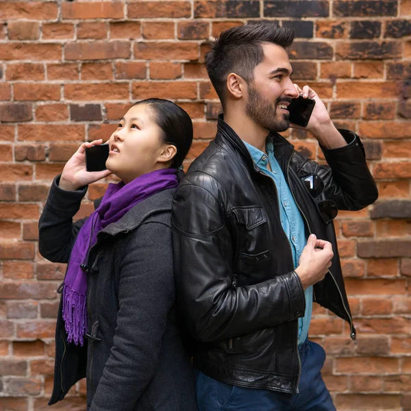 young man and woman stand nearby back to back, talking on their