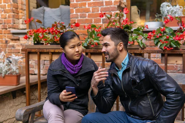 Europeo joven hombre hablando con un asiático chica sosteniendo un smartphone — Foto de Stock