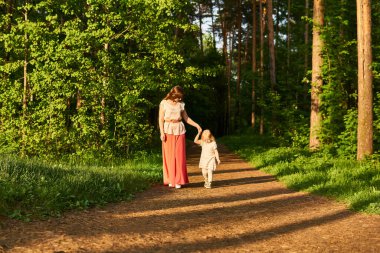 Anne ve küçük kızı akşam parkında yolda yürürler, el ele tutuşurlar.