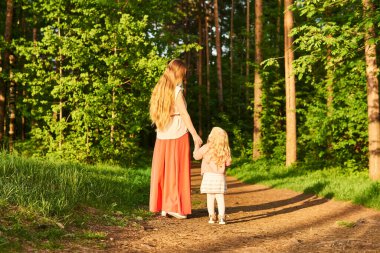 Anne ve küçük kızı akşam parkında yürüyorlar, arkadan bakıyorlar.
