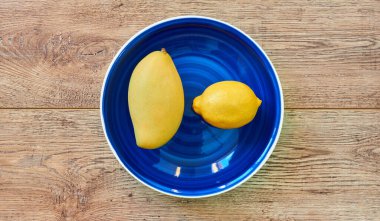 Sarı meyveler - limon ve mango - ahşap bir masanın üstünde mavi bir tabakta