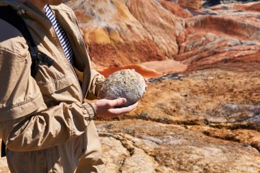 Paleontolog, bir çöl manzarasının arka planında dinozor fosil yumurtası tutuyor. Yakın plan.