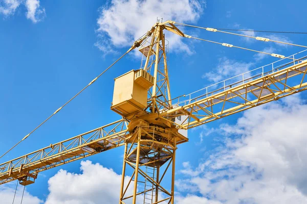 fragment of a yellow construction tower crane against a blue sky with clouds