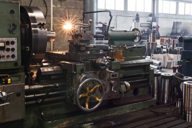 Ön planda torna tezgahı olan bir fabrika binasının içi.