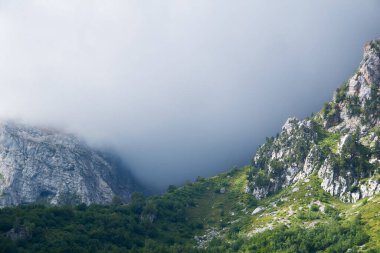 Dağ manzarası. Güneşin aydınlattığı kayalık bir geçit ve arkasında kasvetli bir bulut.