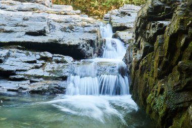 Kayaların arasındaki bir derede küçük bir şelale, su jetleri hareket halinde bulanıklaşır.