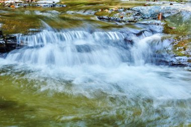 Kayaların arasındaki bir derede küçük bir şelale, su jetleri hareket halinde bulanıklaşır.