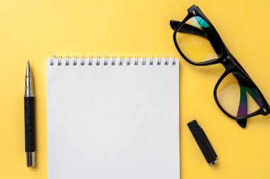 Parlak sarı arka planda defter, gözlük ve Ofis Kırtasiye