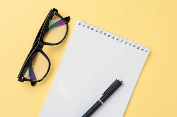 Notebook, eyeglasses and office stationery on bright yellow background