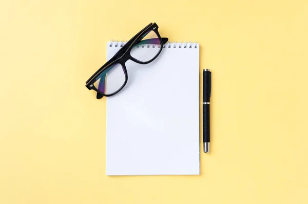 Notebook, eyeglasses and office stationery on bright yellow background