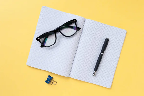 Notebook, eyeglasses and office stationery on bright yellow background