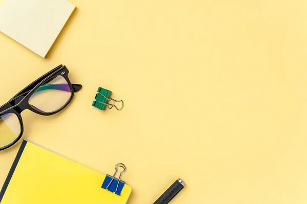 Caderno, óculos e artigos de escritório sobre fundo amarelo brilhante — Fotografia de Stock