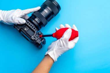 Top view female hand wearing white gloves cleaning up dslr camera with air dust blower clipart